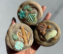Load image into Gallery viewer, 3 rustic looking soap rounds with cactus and flower embeds in the center of each bar.  Each soap top is textured to help give dimension to the soap.