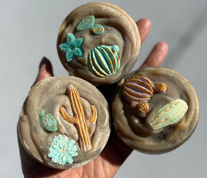 3 rustic looking soap rounds with cactus and flower embeds in the center of each bar.  Each soap top is textured to help give dimension to the soap.