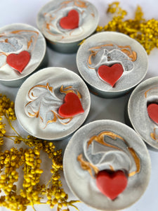 Six frosted grey soaps with red hearts and gold mica  are surrounded by chamomile flowers 